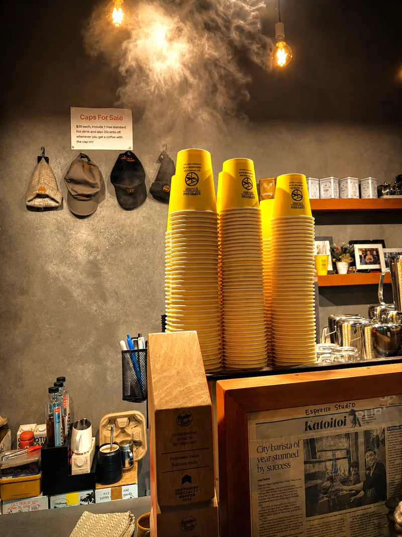 Tall stacks of yellow Espresso Studio cups beneath warm lights