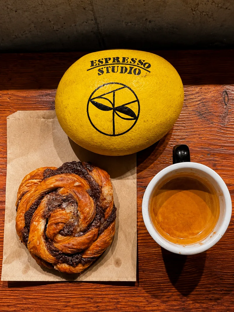 Espresso Studio branded yellow object, pastry and coffee on a wooden table