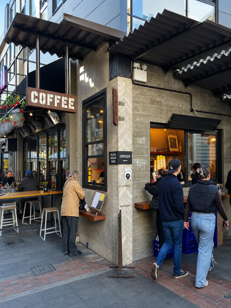 Customers at an outdoor coffee counter beneath an illuminated coffee sign